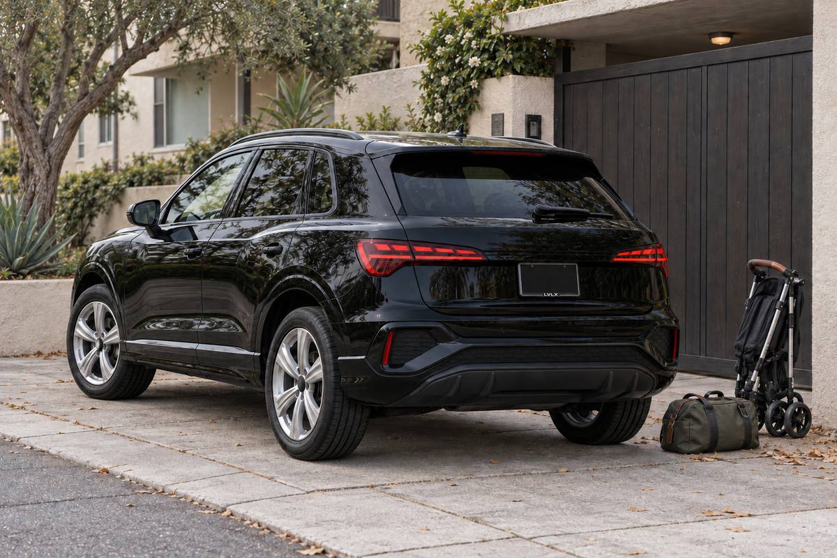 Black Audi Q3-style SUV with a folded stroller and bag beside a garage.