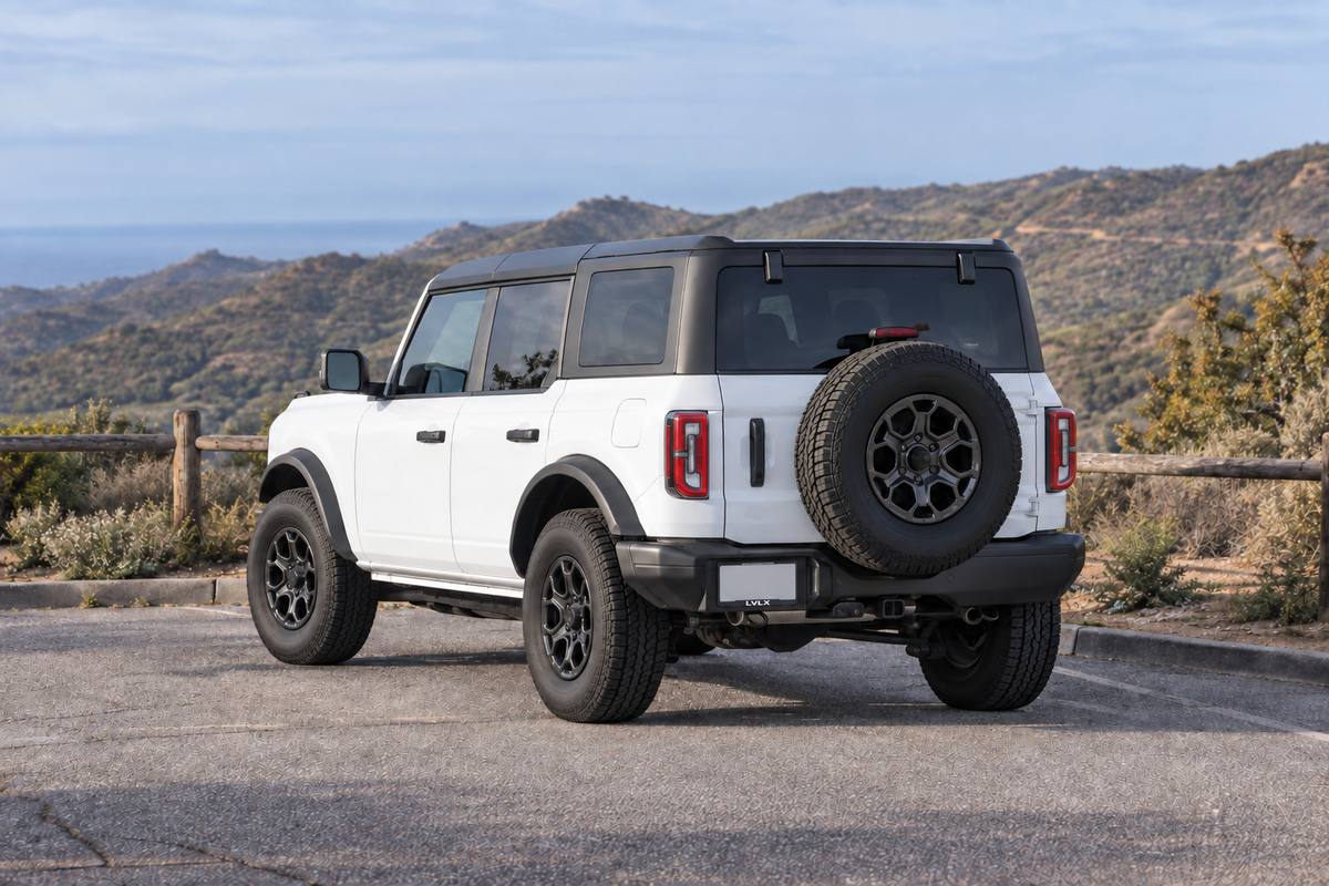 White four-door Bronco with a hardtop and spare tire at a paved canyon turnout.