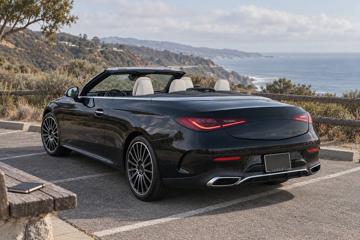 Black convertible on a paved coastal overlook with ocean cliffs in the background.