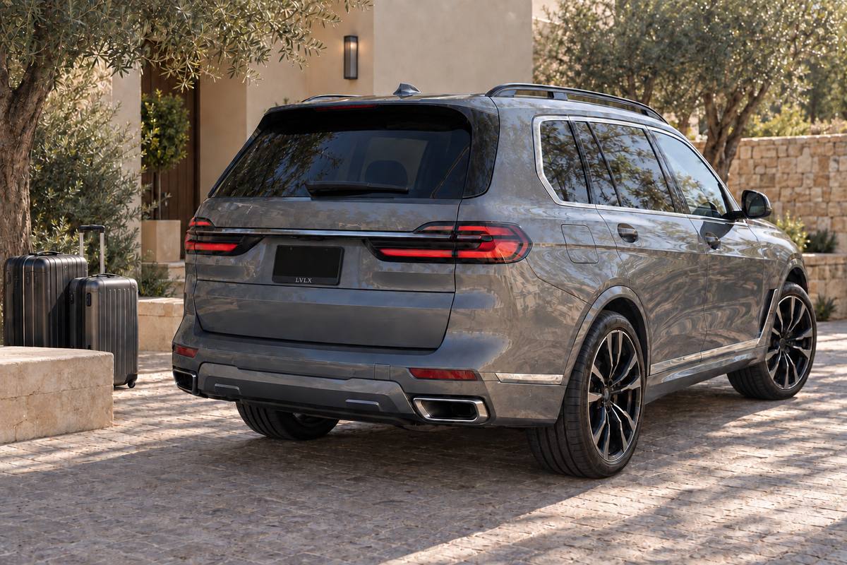 Large gray SUV and suitcases on a shaded stone driveway.