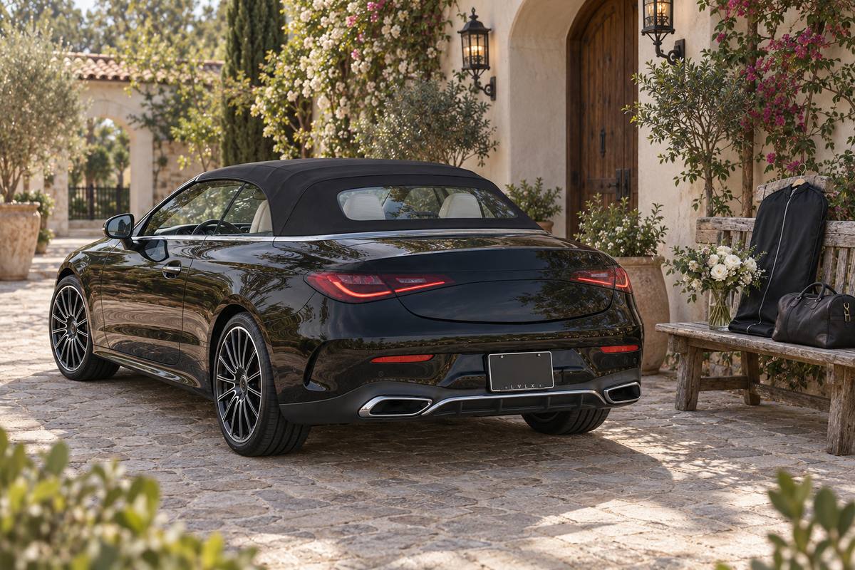 Black soft-top convertible with a garment bag and flowers in a vase at a courtyard entrance.
